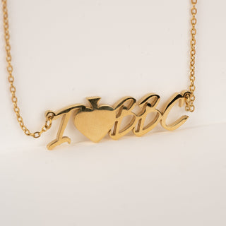 I heart BBC gold necklace on plain white backdrop.