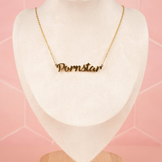 The gold "Pornstar" necklace with delicate cursive lettering is displayed on a mannequin. The chain drapes gracefully around the neck, highlighting its elegant shine.