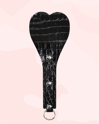 Black crocodile-patterned paddle with silver accents on a pink background