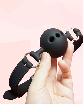 The Velvet Bit Ball Gag being held in a hand, it shows a close up of the silicone ball with air holes.