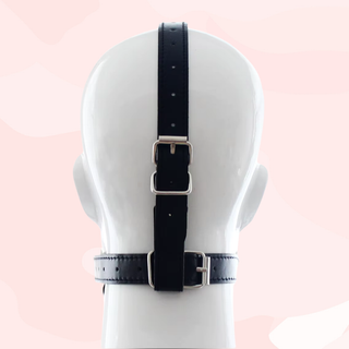 Black leather harness with silver buckles on a mannequin head against a pink background