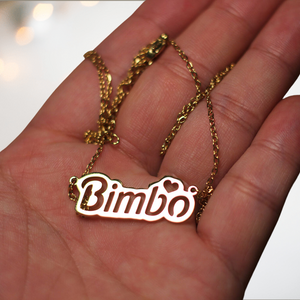 A close up of the Bimbo necklace from House Of Chastity being held in the palm of a hand, you can see that the pendant is in gold, with the lettering cut out.