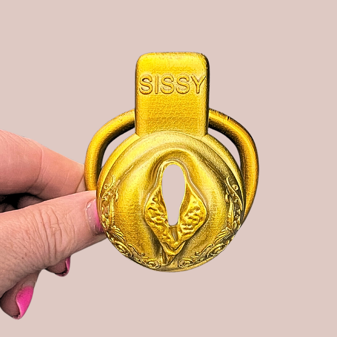 A front view of the Gold Ornate Scroll Sissy Pussy Chastity Cage from House Of Chastity, it is shown here with the 42 mm base ring attached, it is just visible in the background. You can see the SISSY lettering in capitals across the top.