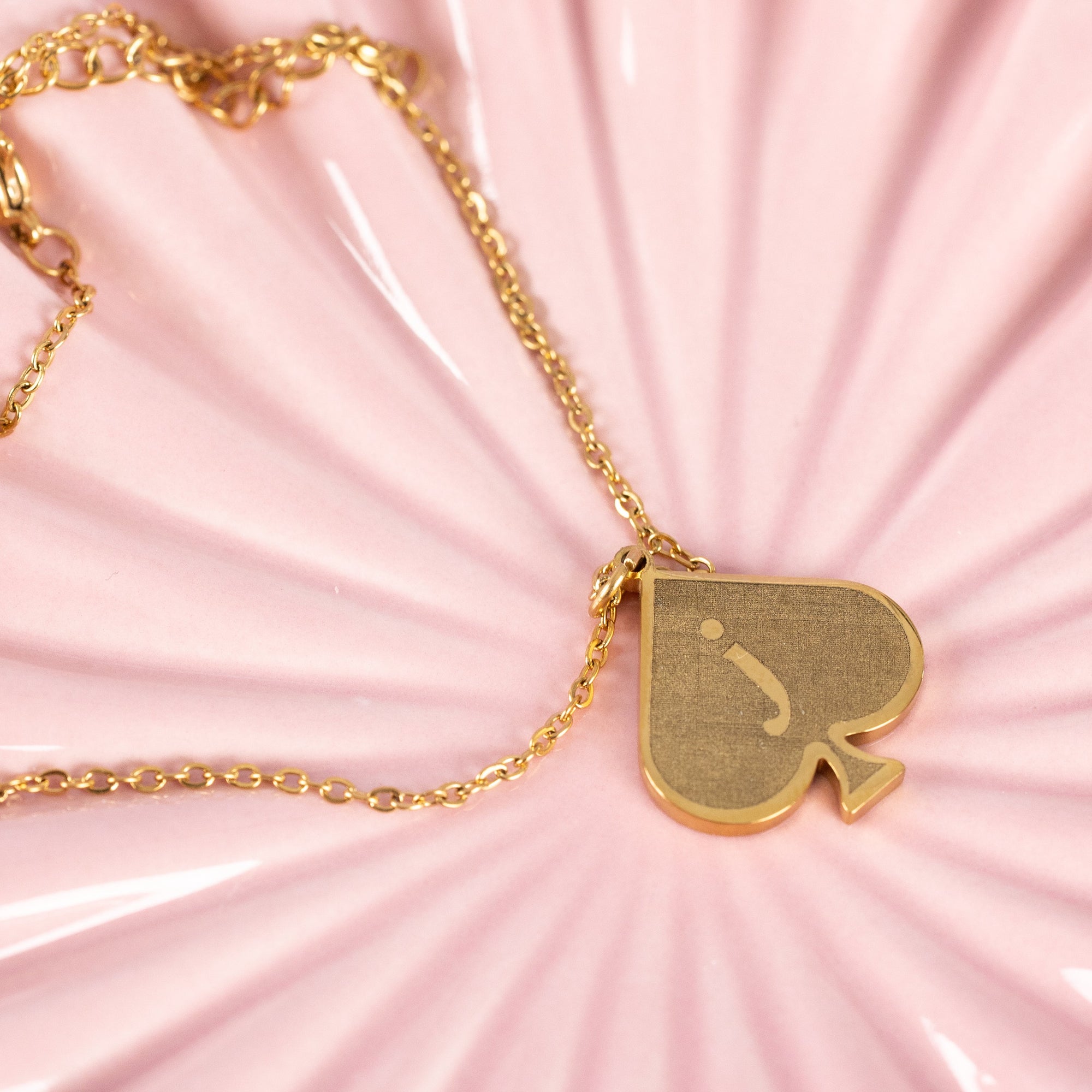 Close-up image of the Jack of Spades bracelet/anklet on a pink background, showcasing the intricate details of the chain and glow of the pendant 