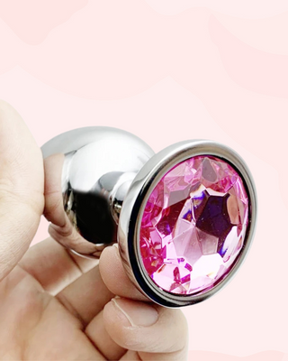 Butt plug with pink gemstone held by a hand on a light pink background