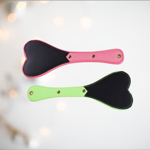 This image of the Luminous Spanking paddles shows the green and pink paddles on offer, you can see the heart shaped head and narrow handle.