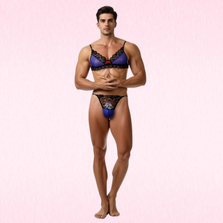 A male model wearing  Luna Lace Duo blue and black lace lingerie set, consisting of a bra and matching briefs, standing against a light pink textured background.