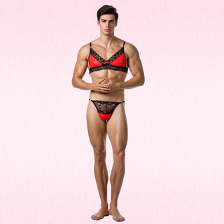 A male model wearing  Luna Lace Duo red and black lace lingerie set, consisting of a bra and matching briefs, standing against a light pink textured background.