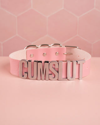 A picture of the cumslut collar in pink showing text on the front.