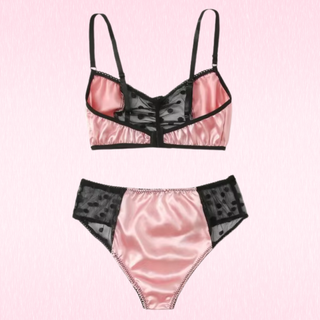 A two-piece lingerie set featuring a satin pink bralette with black mesh panels and trim, and matching high-waisted briefs, displayed on a light pink textured background.