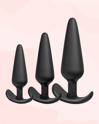 Three individually sized black silicone butt plugs on a pink background