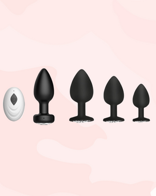 The image shows the vibrating anal plug with its remote control and the three other non vibrating anal plugs in small, medium and large. They are black with a diamond style crystal base gem stone.