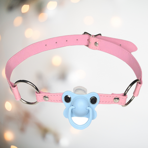 A pink pvc long gag that has a pale babu blue  dummy fixed to the front which the wearer will have to hold in their mouth and a silver buckle fastening to the back. 