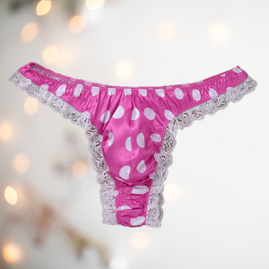 A bright pink satin men's female style knickers. They have a white spot pattern on the bright pink fabric, white lace edging to the legs and a thong style back.