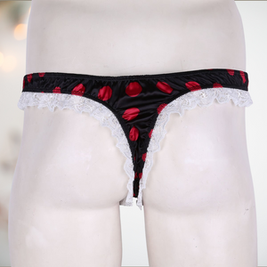 A black satin men's female style knickers. They have a red spot pattern on the black fabric, white lace edging to the legs and a thong style back.