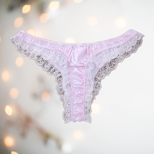 A soft pale pink satin mens female style knickers. They have a white spot design on the pink fabric, white lace edging to the legs and a thong style back. 