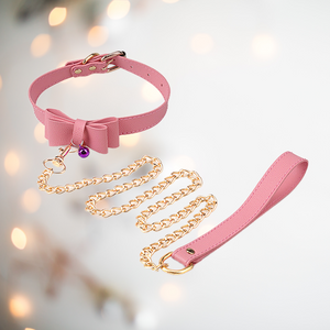 A pink choker neck collar with buckle fastening, has a decorative bow to the front with a small coloured bell, it also comes with a gold chain lead. 