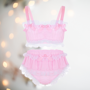 In baby pink, this bra and panties set has bandeau style bra top edged in white lace and colour matching satin bows. The panties are a high waisted design and have matching lace frills and satin bows.