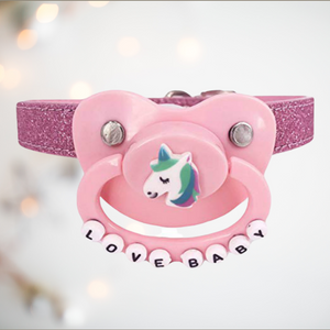 The pink unicorn pacifier gag shown close up, you can see the unicorn image on the front and the Love Baby Lettering on the handle.